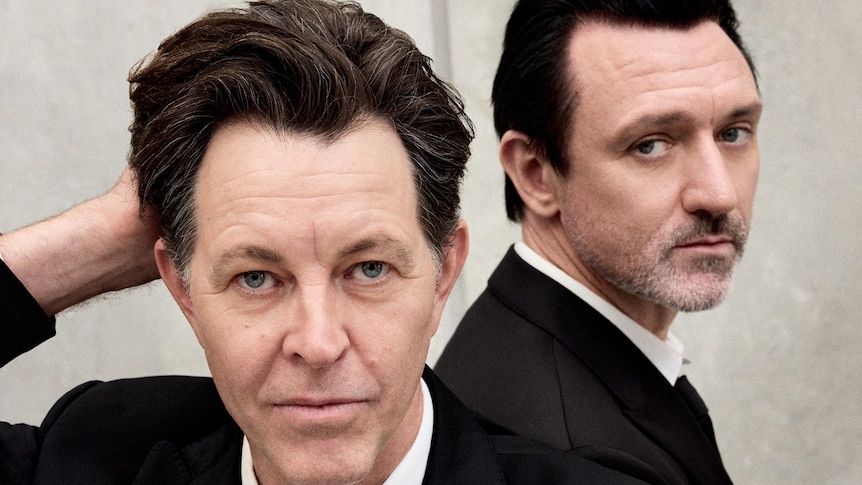 Powderfinger frontman Bernard Fanning and Something For Kate frontman Paul Dempsey pose in black suits.