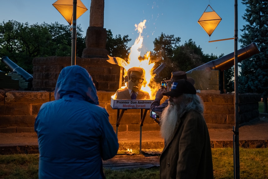 Two men watch an effigy of Daniel Andrews burning in the early hours of the morning.