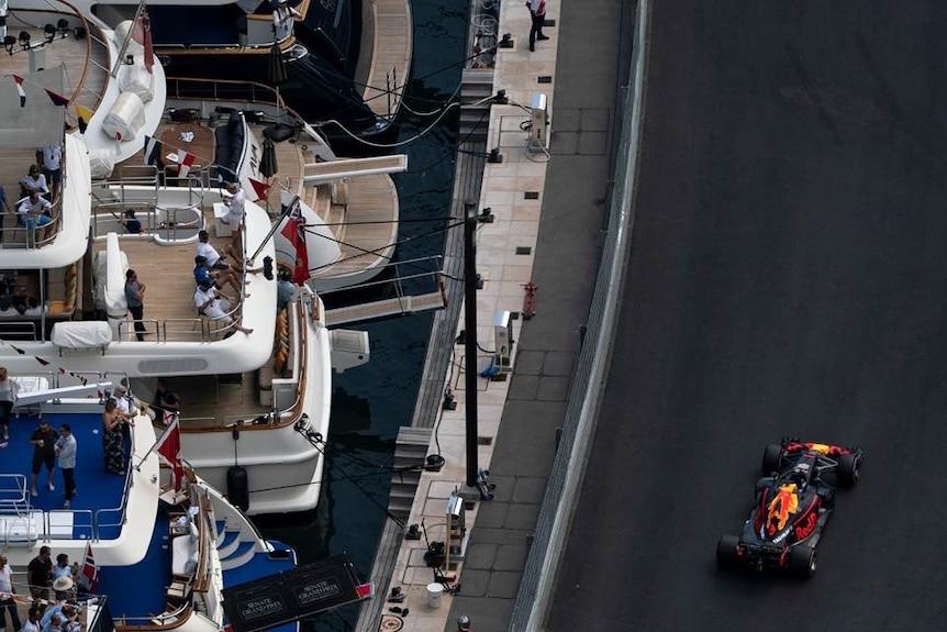 The Red Bull of Daniel Ricciardo drives past a series of yachts on Monaco Harbour with interested spectators watching on.