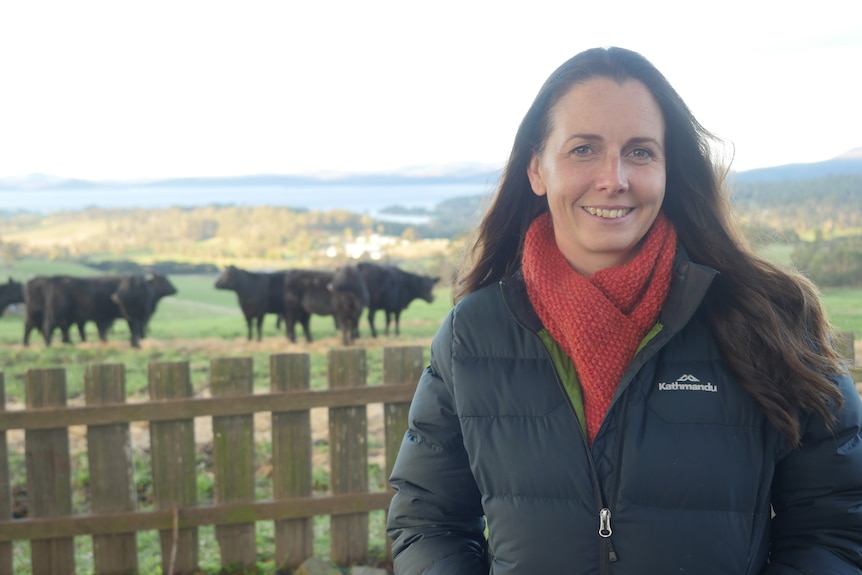 A woman smiles in front of a paddock of cows