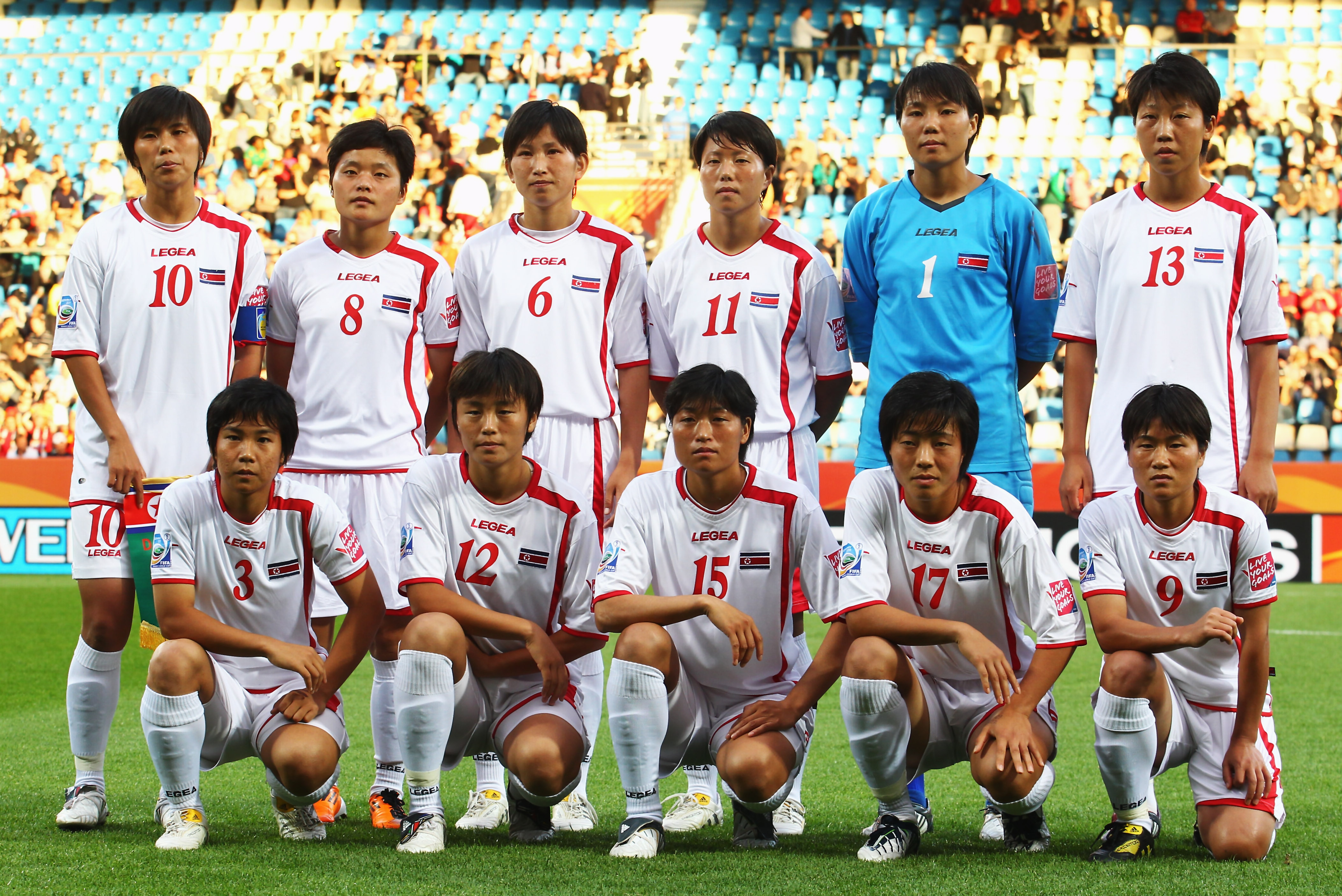 A women's soccer team wearing red and white pose for a photo with a crowd behind them before a game