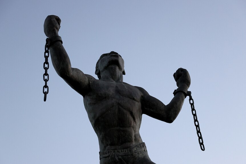 A statue of a slave breaking his chains off, hands high in the air