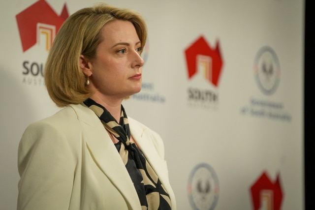 Uma foto lateral de uma mulher com uma expressão séria em frente a uma placa do governo sul-africano.