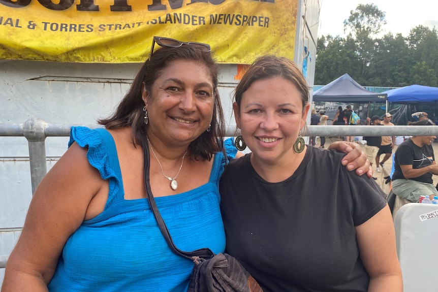 Two women arm-in-arm infront of a Koori Mail banner.