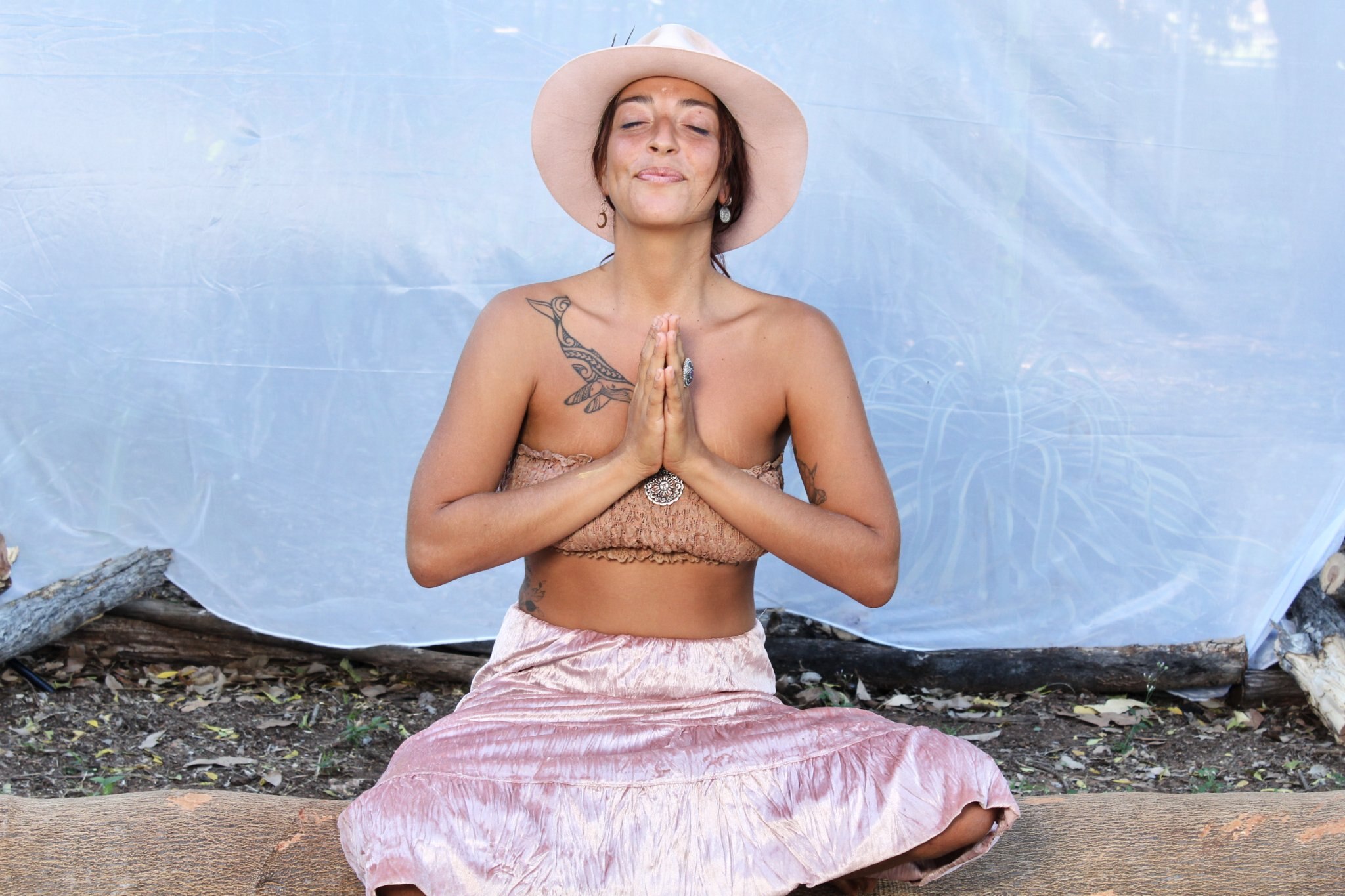 A young woman in a hat and a tube top sitting in front of a tarpaulin, with her hands folded