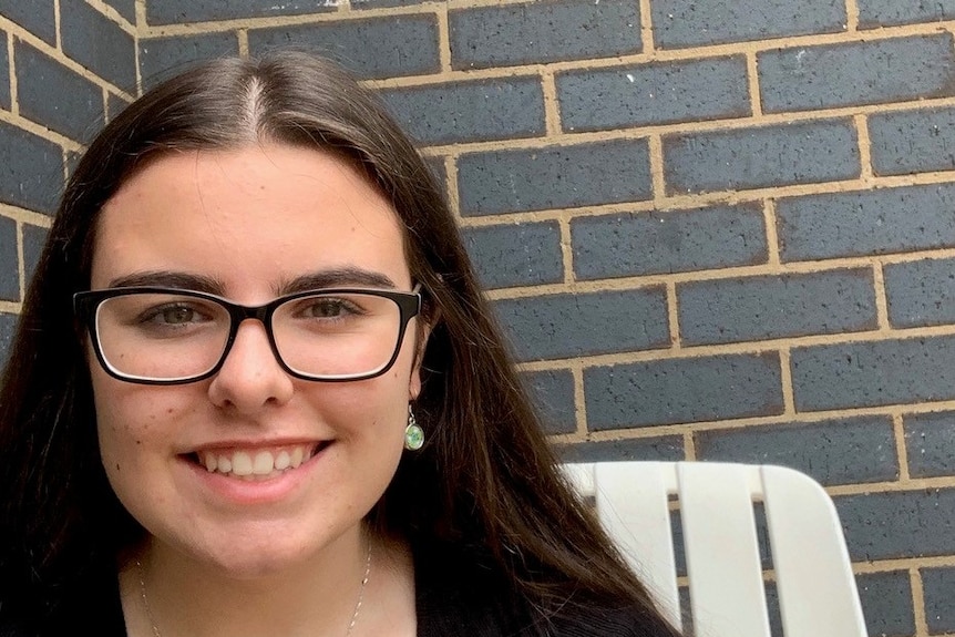 High school student Elaine Greeley sitting in front of a grey brick wall.