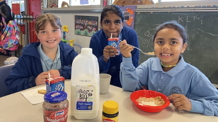 three primary school aged girls sitting at a table eating cereal