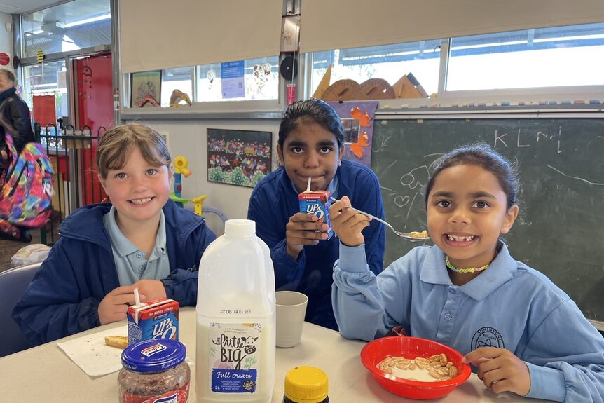 three primary school aged girls sitting at a table eating cereal
