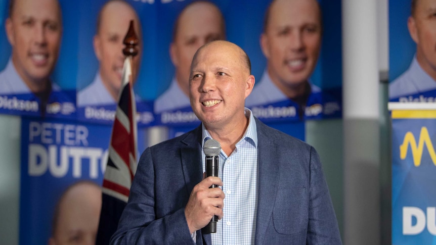 Peter Dutton holds a microphone and smiles as he claims victory in the seat of Dickson.