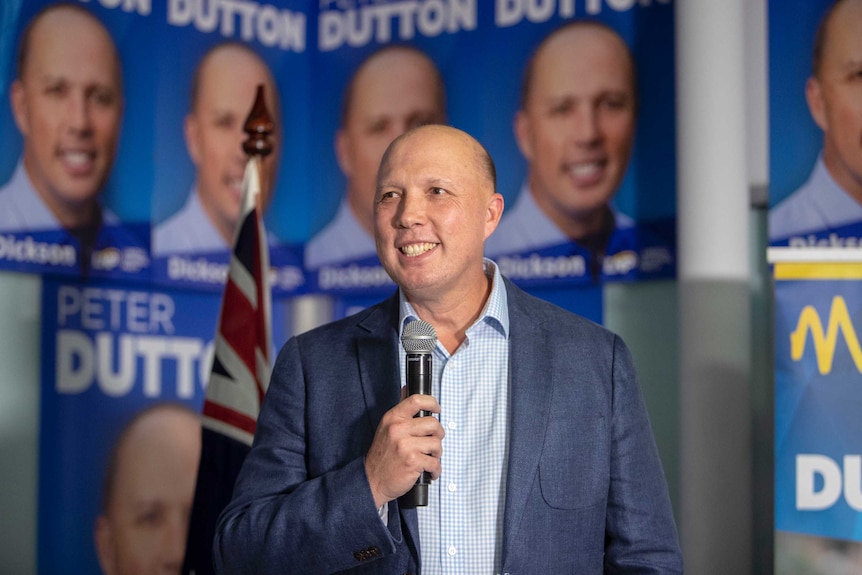 Peter Dutton holds a microphone and smiles as he claims victory in the seat of Dickson.