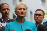 Kerryn Phelps wearing a blue jacket with a red ribbon pin addresses the media with crossbench MPs behind her