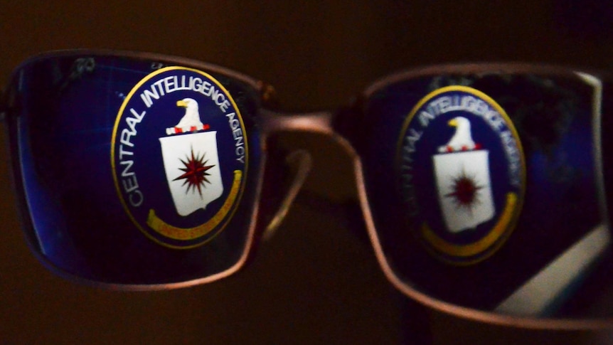 A CIA logo is reflected in glasses.