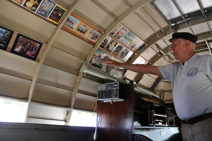 A man points to postcards and pictures on wall of his airbus