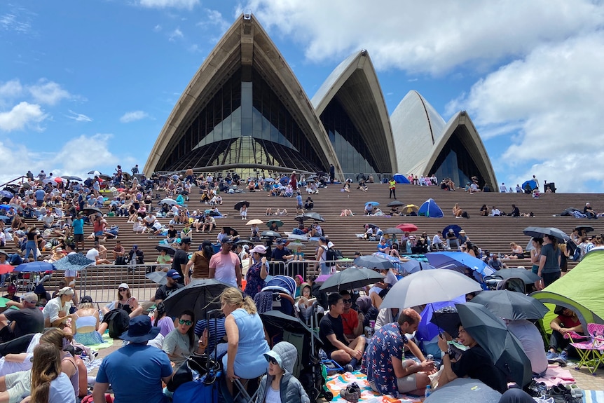 people sitting on picnic rugs at the forecourt of the opera house