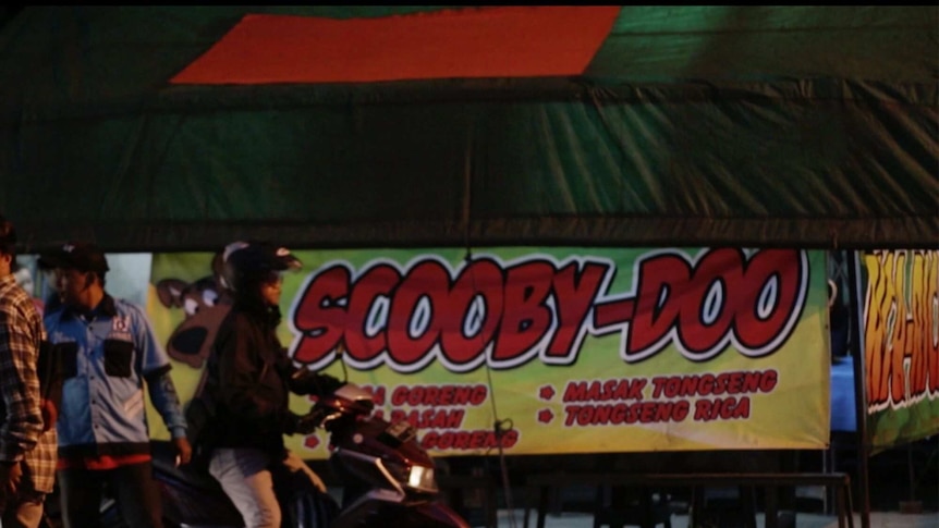 A person on a motorbike rides past a large sign saying "Scooby-doo".