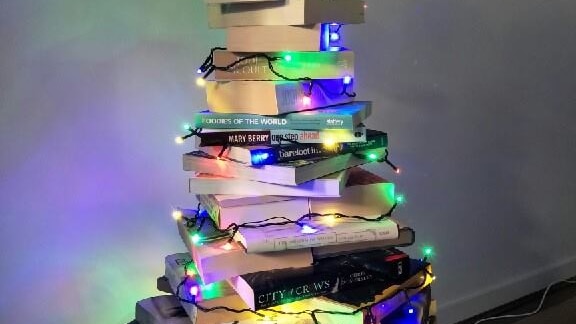Books piled into a pyramid-like shape, draped in coloured fairy lights.