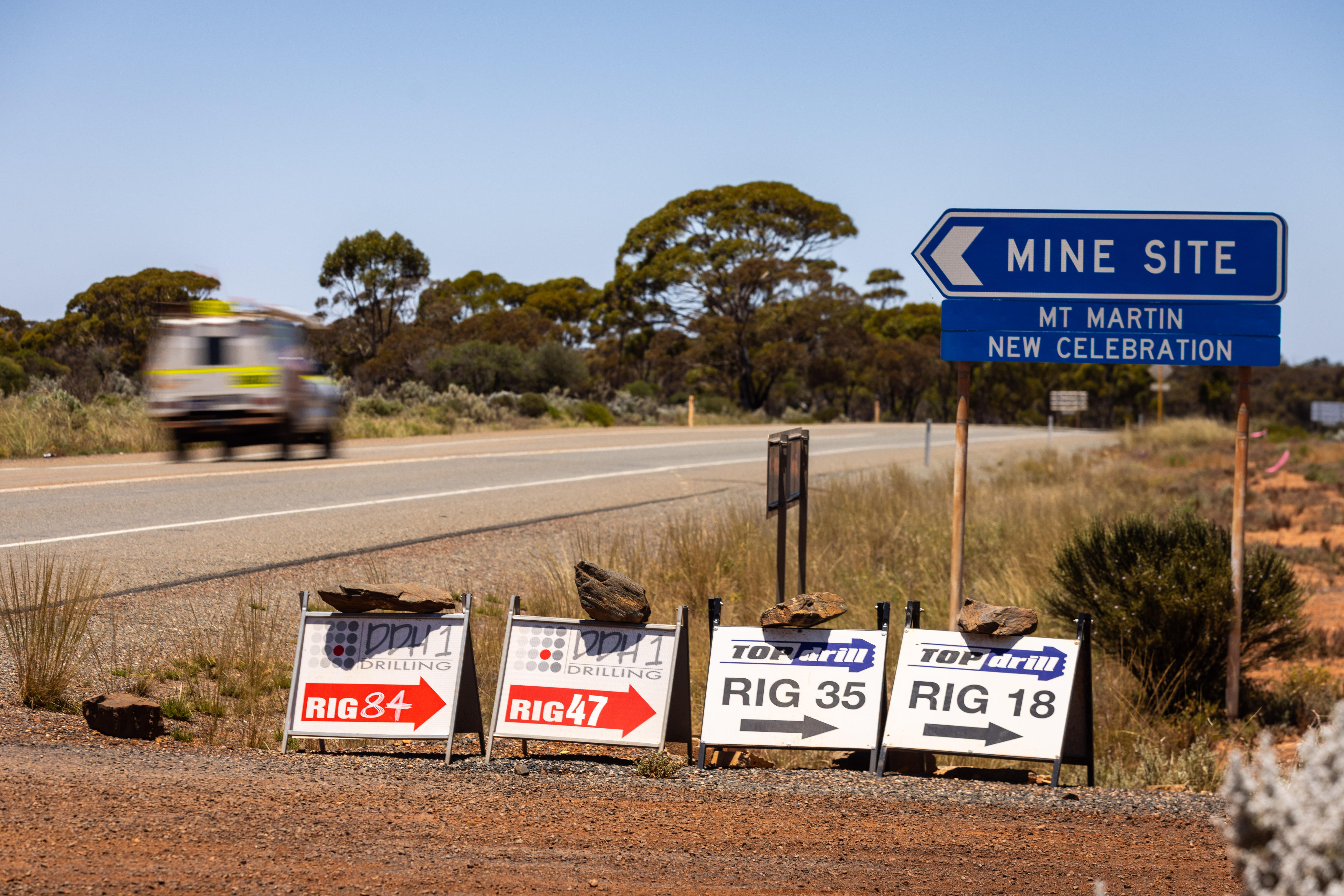 Signs on the side of a road pointing to the location of a working drill rig.  