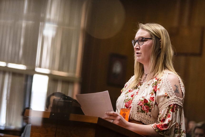 A woman stands at a podium in a court room and speaks