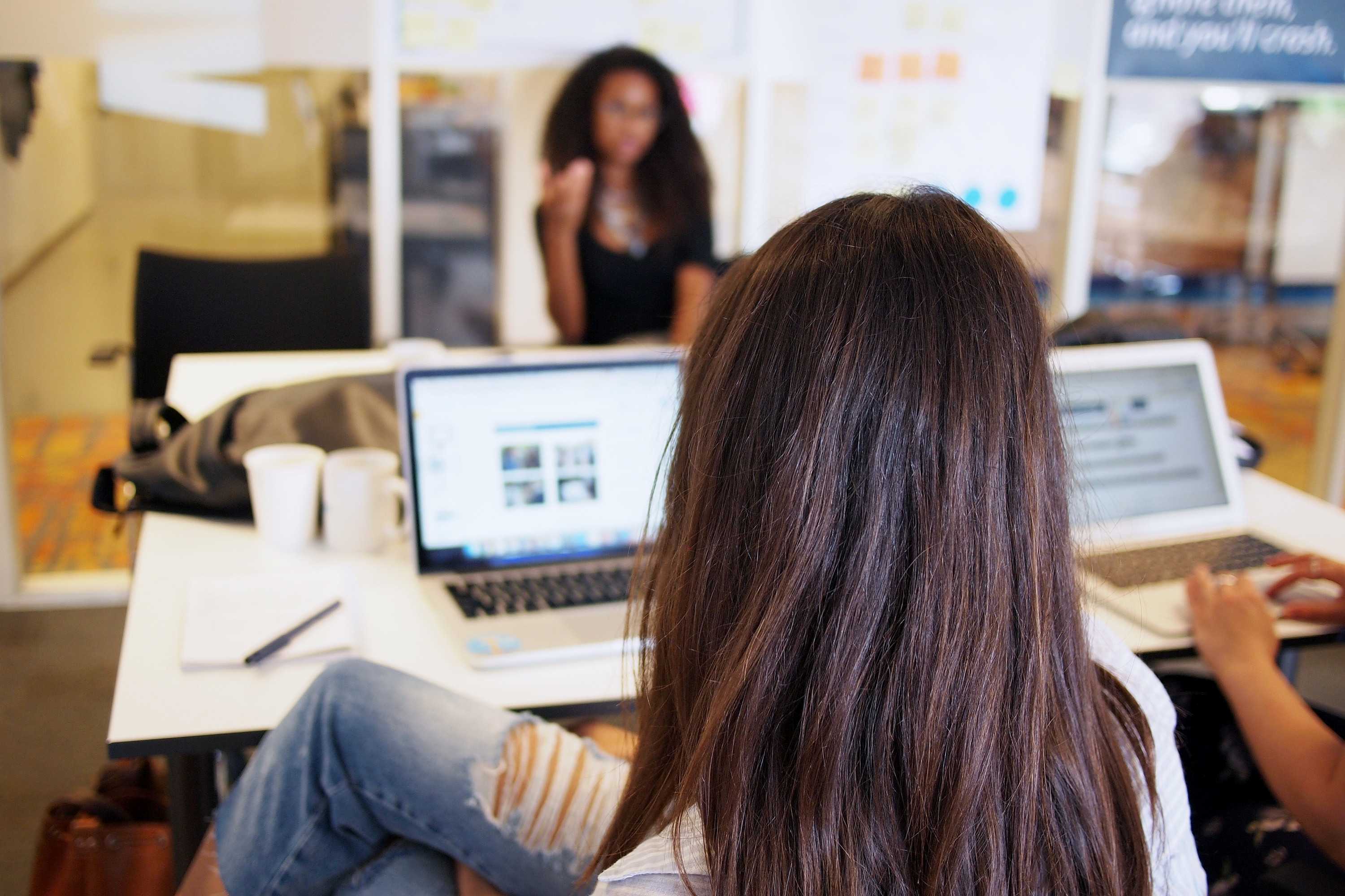 Three women work on laptops in an office.