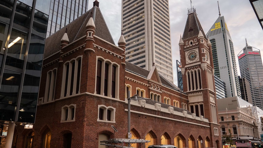 Historic brick town hall building with clocktower surrounded by modern office towers