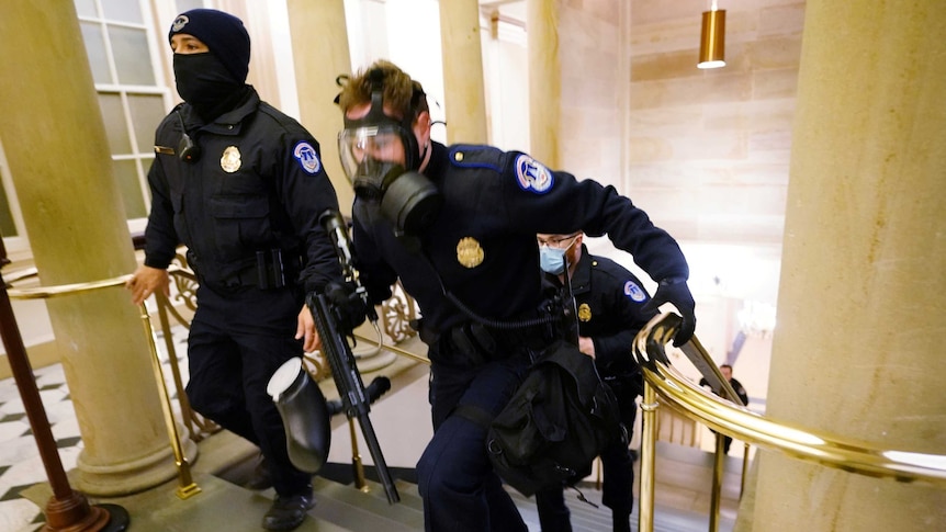Three police officers run up the stairs to take positions as protestors enter the Capitol building.