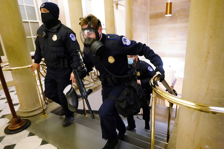 Three police officers run up the stairs to take positions as protestors enter the Capitol building.