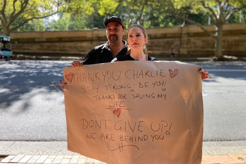 Man and woman stand on the road holding a thank you sign