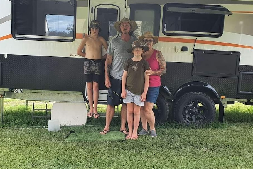 A family of four stand outside their caravan