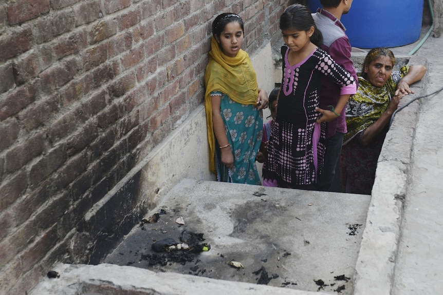Pakistani residents stand at the site where a teenager was burnt alive by her mother.