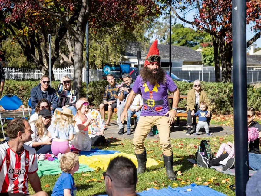 Costa the Gnome telling a story to young children on a lawn.
