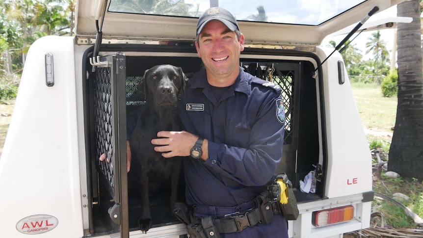 A black labrador is held by a police officer as they both sit at the back of a police vehicle