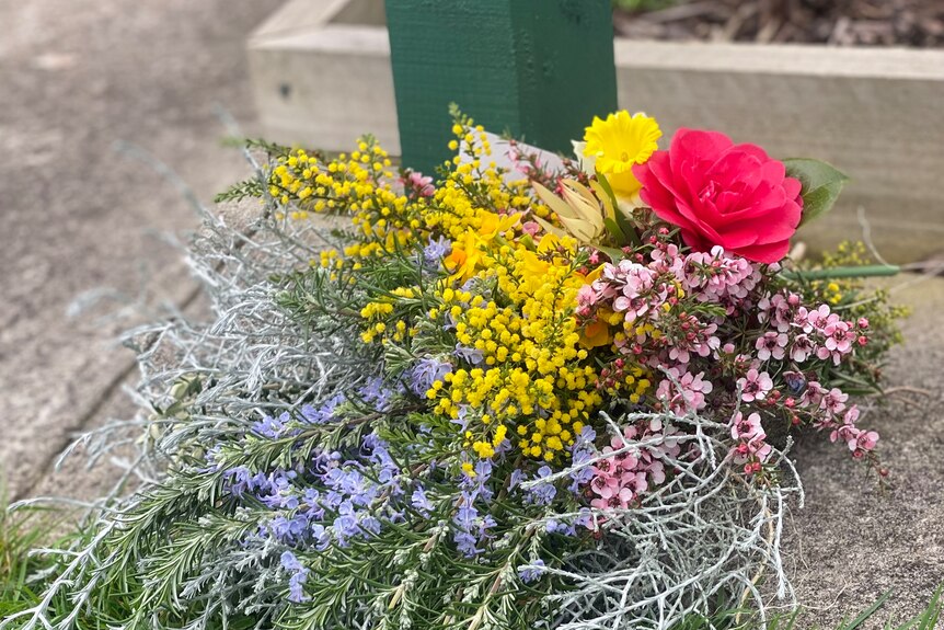 A bunch of flowers including wattle and a rose sit outside a church.