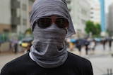 A man with a scarf wrapped around his face and sunglasses obscuring his eyes