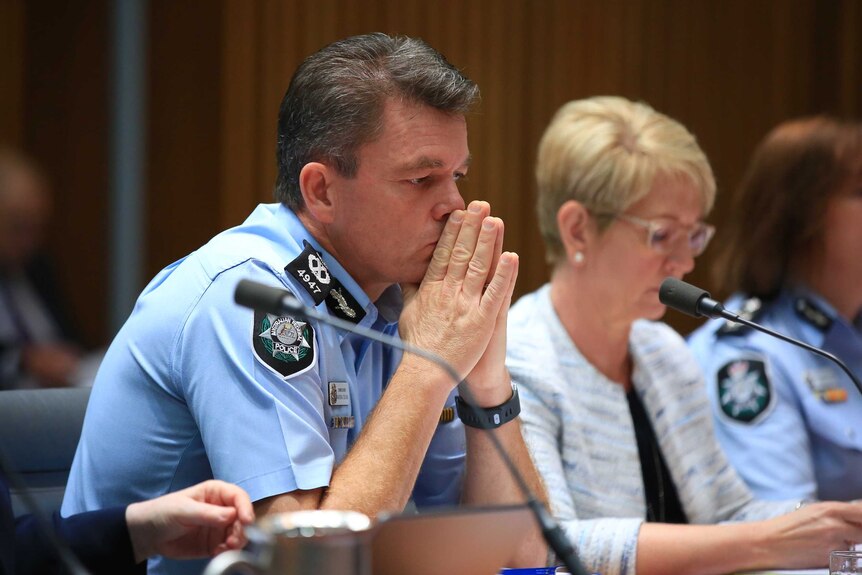 Mr Colvin has his hands pressed together, almost as if he is praying, as he listens in the hearing. He's in uniform.