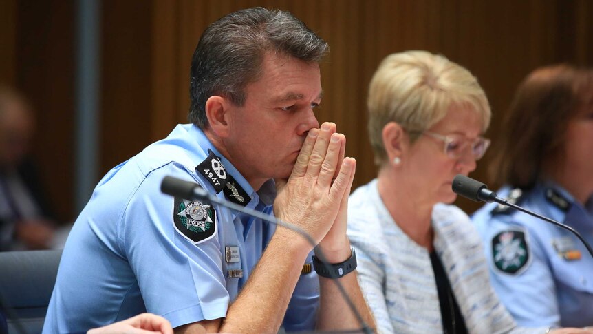 Mr Colvin has his hands pressed together, almost as if he is praying, as he listens in the hearing. He's in uniform.