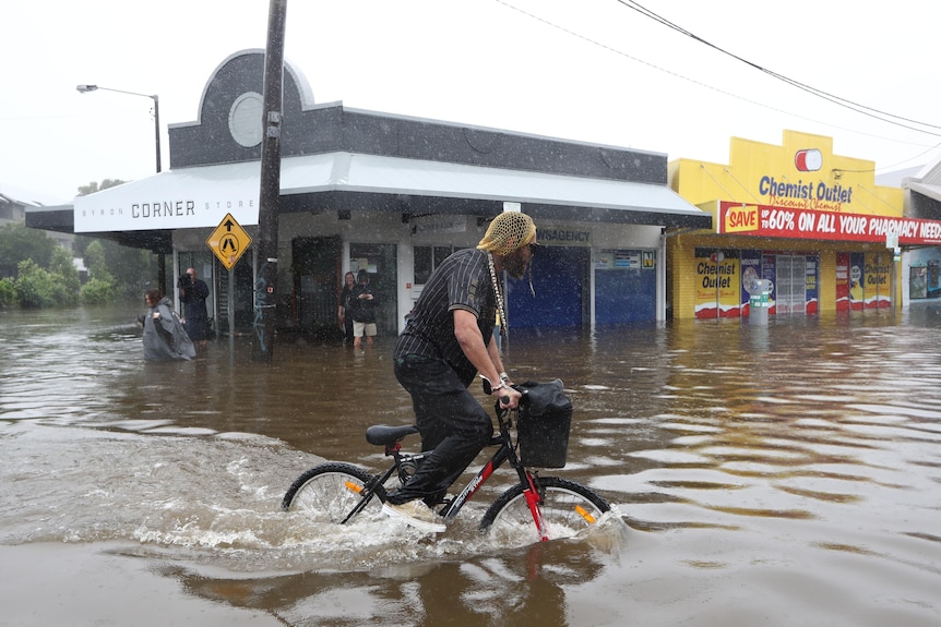 A man rides a bike through flooded Byron Bay