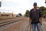A main in jeans, a jersey top and a baseball cap smiles as he stands on one of several railway lines running parallel.