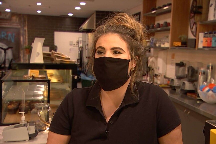 Headshot of a woman wearing a mask at a cafe.