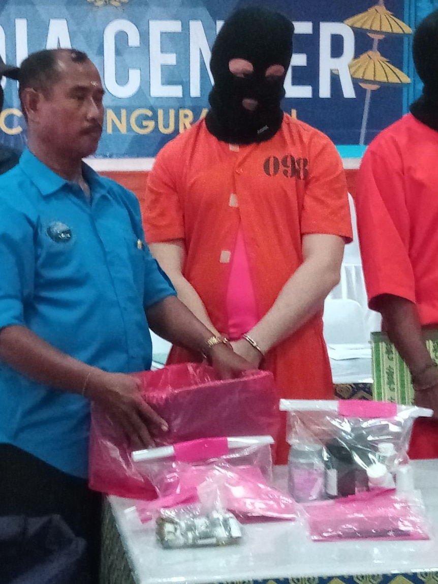 An Australian man wears a black balaclava over his head and an orange jumpsuit.