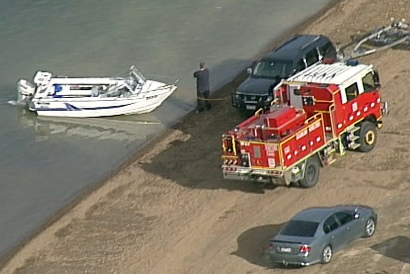 A boat, a vehicle and a fire truck near the edge of the water at Goughs Bay.