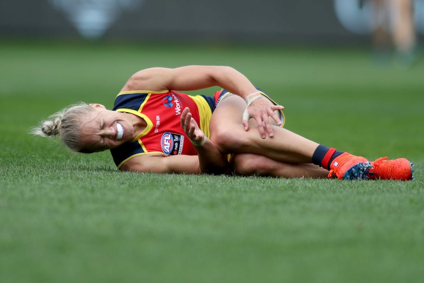 An AFLW player lies on the turf, clutching her knee after being injured in the 2019 grand final.