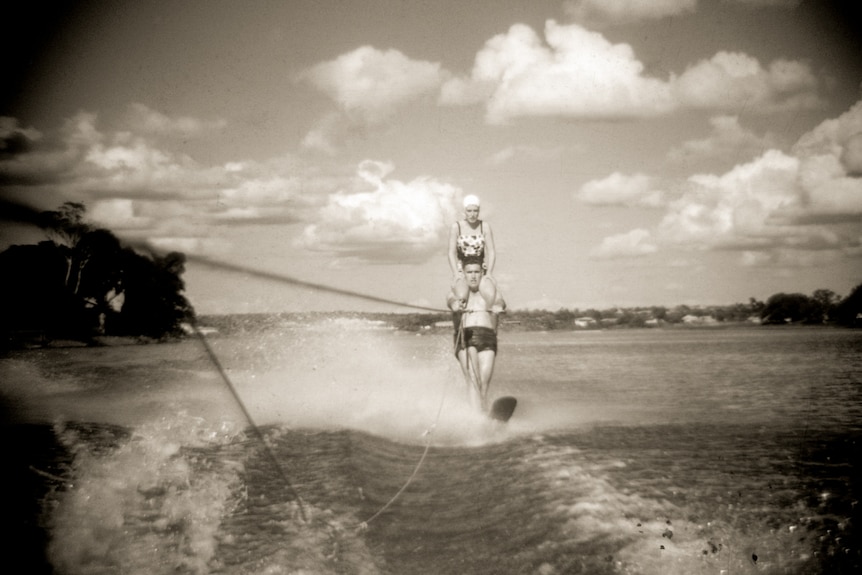 Woman sitting on a man's shoulders who is water skiing.