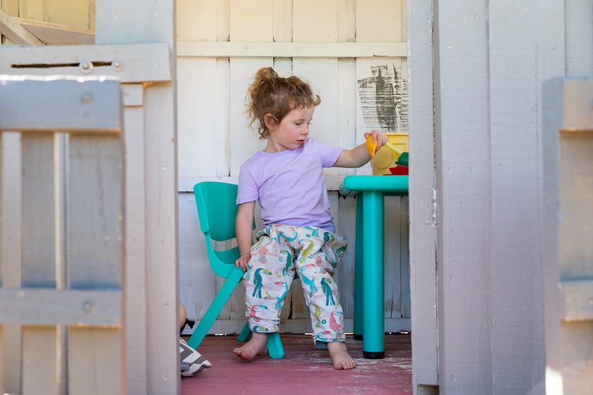 Hayley sits on a plastic blue chair and plays in a cubby house in the backyard. 