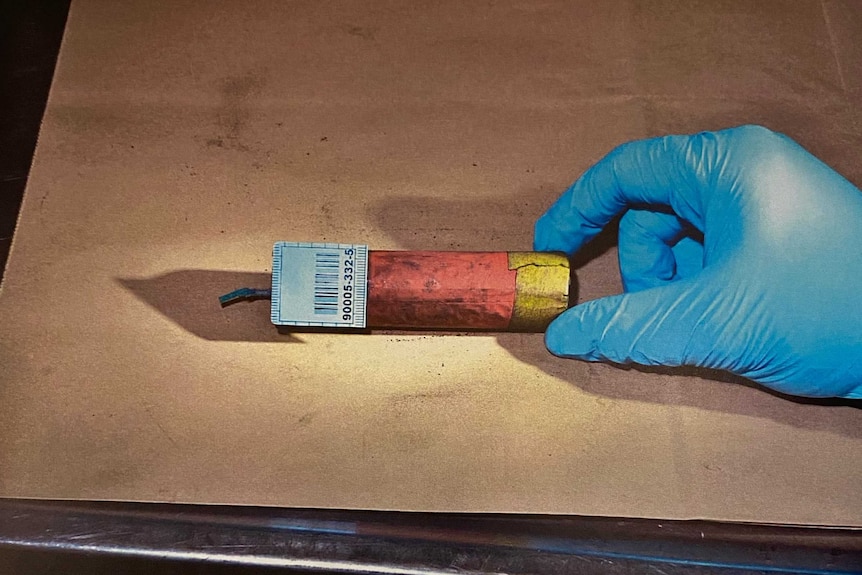 A gloved hand touches a firecracker.