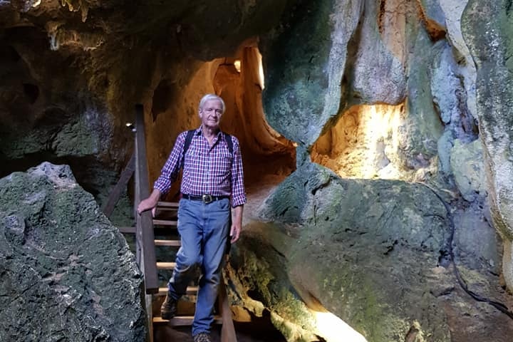 An older man in button up shirt walks down a staircase within a cave.