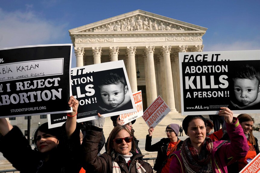 Protesters standing out the front of the US Supreme Court building holding signs which read "Face it...Abortion kills a person"