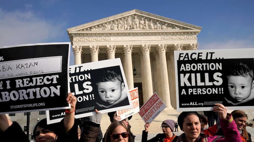Protesters standing out the front of the US Supreme Court building holding signs which read "Face it...Abortion kills a person"