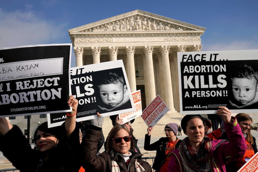 Protesters standing out the front of the US Supreme Court building holding signs which read "Face it...Abortion kills a person"