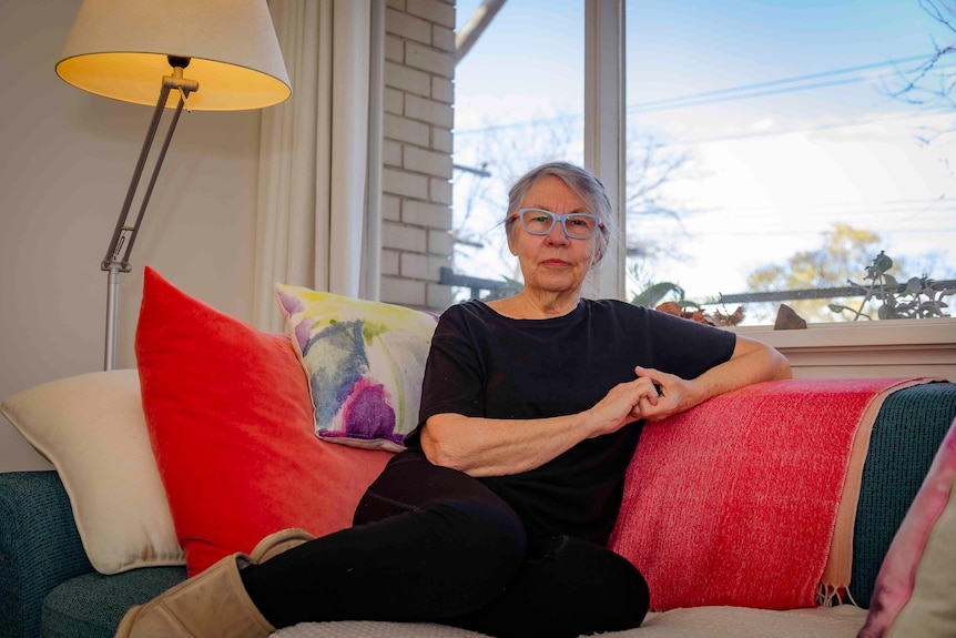 A grey-haired woman curled up on a couch with colorful pillows in ugg boots