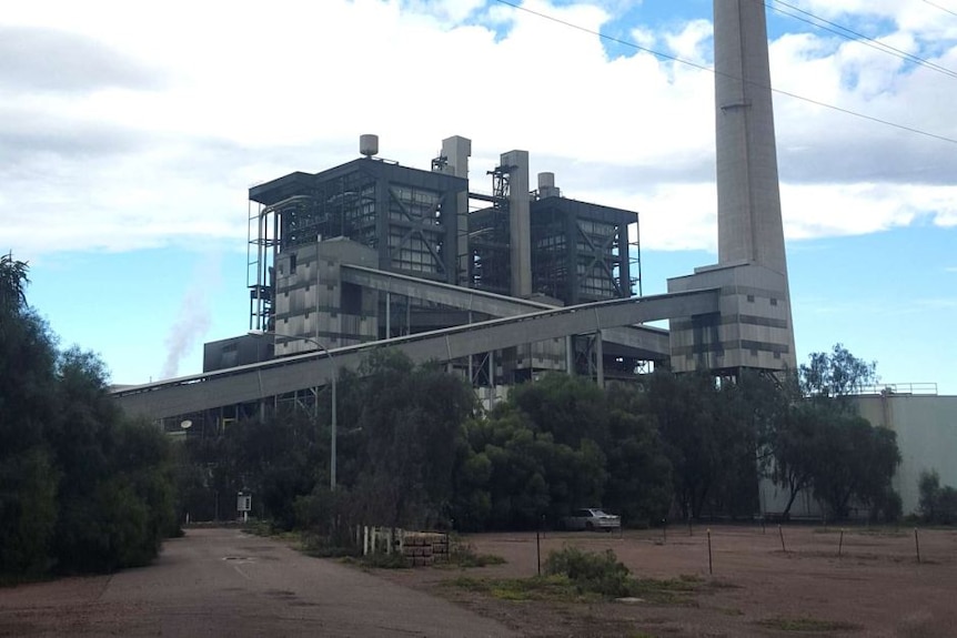 A coal power plant with a tall chimney stack emitting smoke in front of a blue sky and clouds.